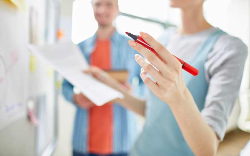Close-up of female analyst holding felt tip pen in hand and speculating about marketing strategy while presenting data of research